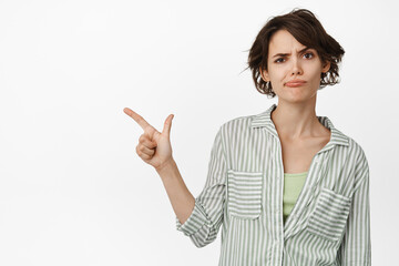 Disappointed frowning girl, pointing finger left, showing smth upsetting, feeling doubtful,...