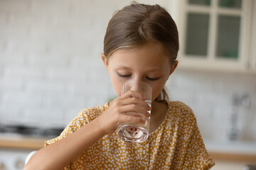 Fototapeta na wymiar Head shot close up of cute little Caucasian girl drinking pure mineral water holding glass at home, preschool child kid enjoying fresh water, dehydration, healthy lifestyle and refreshment concept
