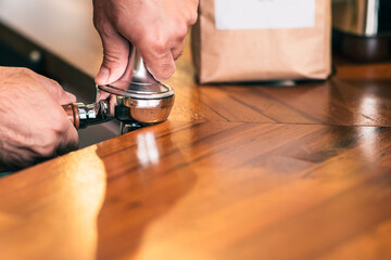 Barista tampering grinded coffee beans to prepare espresso. Includes copy space.