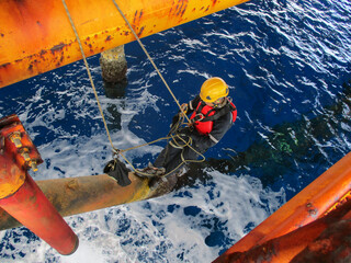 Male worker rope access  inspection of thickness offshore drill yellow