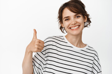 Close up of smiling young woman show thumbs up, like and approve, recommend smth good, excellent choice, standing over white background