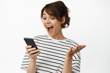 Image of girl looking surprised at mobile phone screen, exciting with great news, notification on...