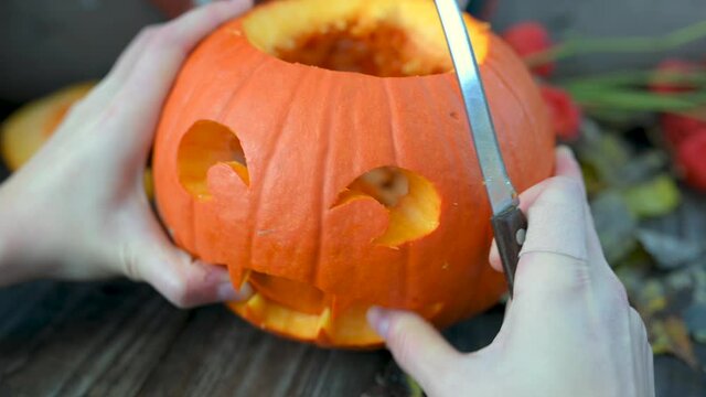 Hands carves a scary halloween pumpkin on a wooden bench in the garden. Making pumpkin decor for Halloween