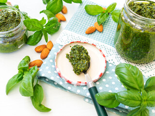 Jar of home made basil pesto and ingredients. Fresh basil leaves and almonds on napkin