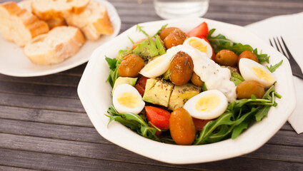 fresh salad of arugula, avocado, cherry tomatoes with olives and quail eggs in white bowl