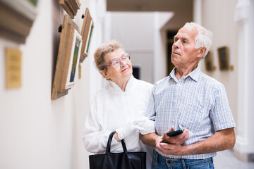 mature European couple examines paintings in an exhibition in hall of art museum