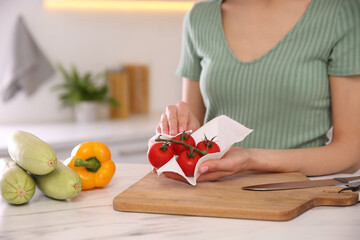 Woman wiping tomatoes with paper towel in kitchen, closeup