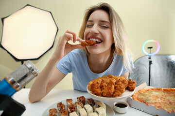 Food blogger eating in front of microphone at table against light background. Mukbang vlog