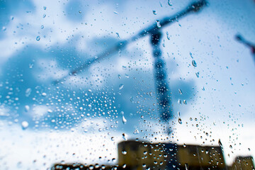 the image of a construction crane in a blur behind the glass with raindrops