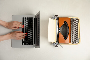 Woman working with laptop near old typewriter at light table, top view. Concept of technology...