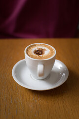 Isolated cup of coffee with foamed milk and brown sugar grains floating at the top over a wooden table.