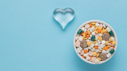 A glass heart and a bowl with pills on a blue background. Flat lay.