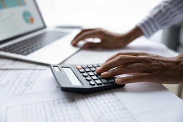 Crop close up of ethnic woman manage budget consider financial paperwork document pay online on computer. African American female calculate expenses on calculator machine. Banking concept.