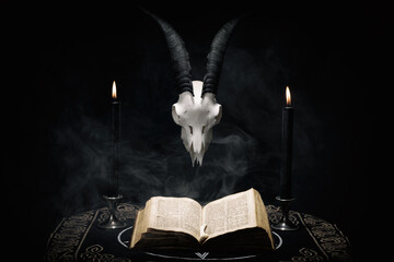 Open old book, goat skull and  black candles on witch table. Occult, esoteric, divination and wicca...