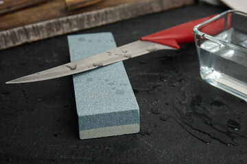 Sharpening stone, knife and water on black table, closeup