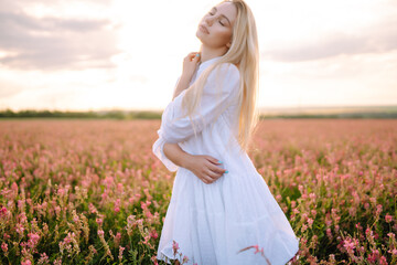 Fototapeta na wymiar Beauty romantic girl Outdoors at sunset. Young woman in stylish clothes posing in the blooming field. Nature, vacation, relax and lifestyle. Fashion concept.