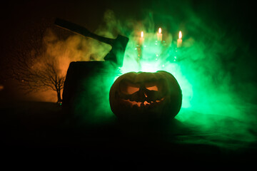Scary orange pumpkin with carved eyes and a smile with burning candles and an ax