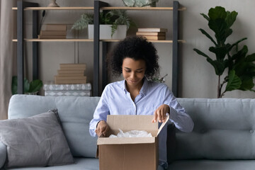 Happy millennial African American female buyer client open unpack box with internet order, buy on...