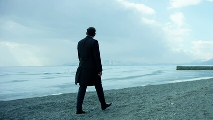 4K Camera follows a lonely businessman walking on the beach near iced lake.  Shot on RED EPIC-W Helium Cinema Camera in Slow Motion. - Powered by Adobe