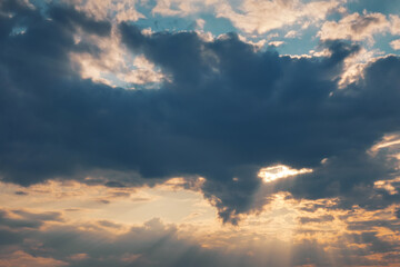 Evening sun shining through thick clouds. Bright view of natural colorful background at sunset.
