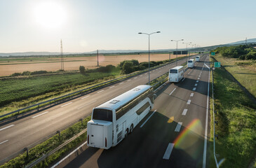 Series of modern White buses departing on a wide highway in a rural backdrop. Convoy of buses....
