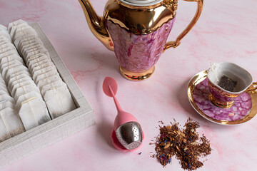 teapot and pink tea cup with tea bags and tea infuser ball