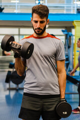 young hispanic latino man in the gym doing biceps with weights. vertical photo