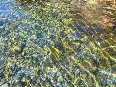 Gravel pebbles beach. Crystal clear sea water. Transparent calm sea. Colorful stones on the seabed. Sunshine on the ripples water. Beautiful seascape. Zen, relax, meditation on Mediterranean coast.