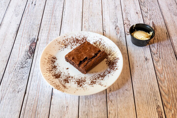 Square dessert portion of chocolate brownie cake with nuts, cocoa powder and vanilla ice cream
