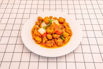 Popular Chinese restaurant recipe of sweet and sour pork with roasted vegetables on white plate and checkered tablecloth