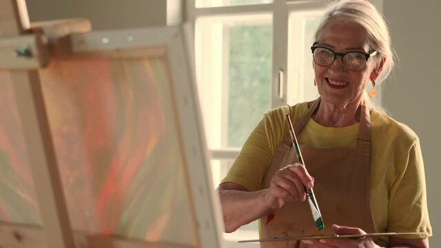 Senior Artist, Art Workshop, Sun Rays, Painting Woman. Happy senior woman artist paints a picture on canvas