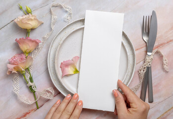 Hands holding wedding menu over a ceramic plate on a marble table