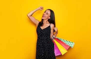 Beautiful happy young stylish brunette woman in a dress is posing with many colorful shopping bags and having fun