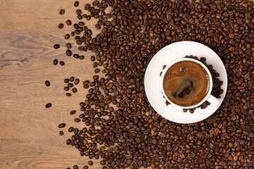 White coffee cup and saucer on wooden background with roasted coffee beans.