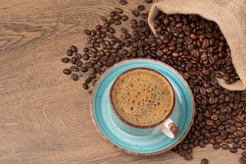 Coffee cup and saucer on wooden background with roasted coffee beans in a burlap sack.