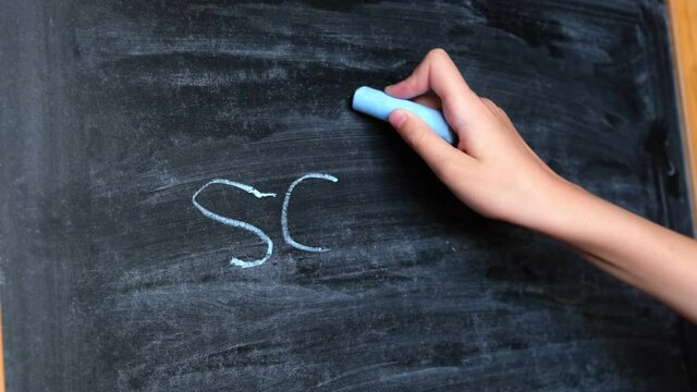 Child Hand Erases Lettering From the Blackboard. Hand of Little Pupil erases School from Chalkboard. Back to School. Education and Elementary School Concept. Close up Back View.