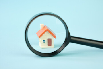 Small house under a magnifying glass. Real estate search concept, purchase and sale of housing, rent, insurance.
