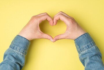 Obraz premium First person top view photo of woman's hands showing heart sign with fingers on isolated yellow background with copyspace