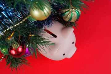 piggy bank pig under a christmas tree decorated with christmas balls and tinsel on a red background, close-up, top view .