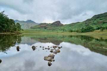 Langdale Pikes reflected in Blea Tarn, with small boulders in the foreground