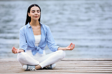 Young woman meditating near river. Space for text