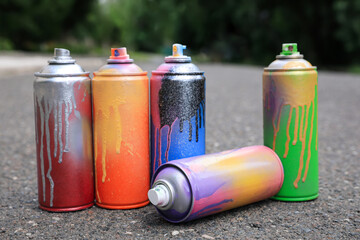 Used cans of spray paint on asphalt road. Graffiti supplies - obrazy, fototapety, plakaty