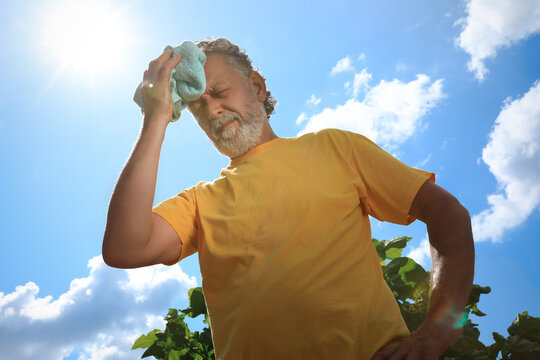 Senior man with towel suffering from heat stroke outdoors, low angle view