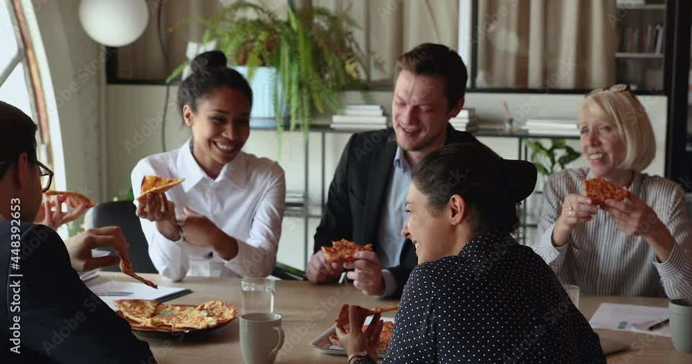 Wall mural young indian woman and colleagues eat pizza during lunch break in office. multi racial employees enj