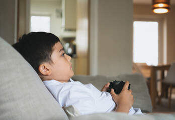 Portrait of happy kid holding video game or game console. Smiling Child playing game online at home, Young boy siting sofa having fun and relaxing on his own on weekend,New normal lifestyle concept