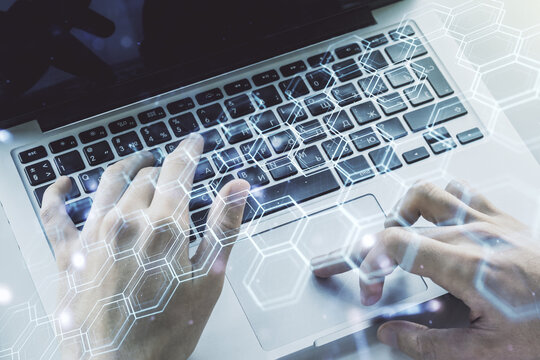 Creative concept of wireless technology with hexagon hologram and hands typing on laptop on background. Big data and database concept. Multiexposure