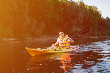 Handsome man in orange life jacket kayaking on a river next to a shore