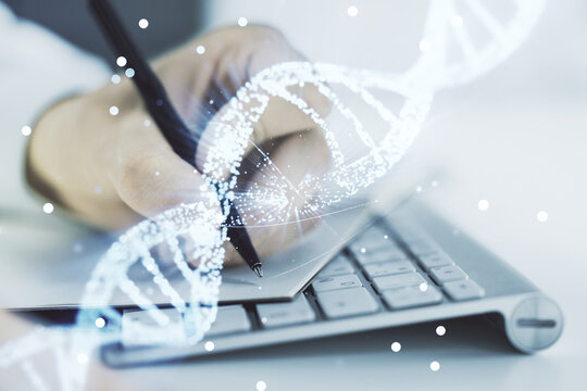 Double exposure of creative DNA hologram and hand writing in notebook on background with laptop. Bio Engineering and DNA Research concept