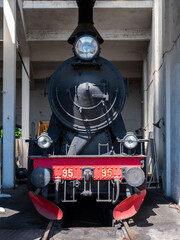 Front of steam locomotive with black and red metal on rail track in a garage