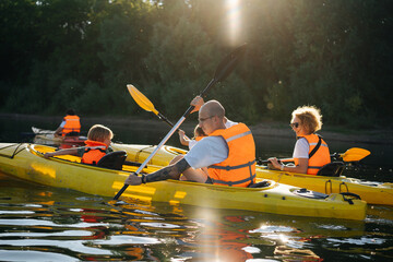 Family in orange life jackets kayaking on two boats on a river.